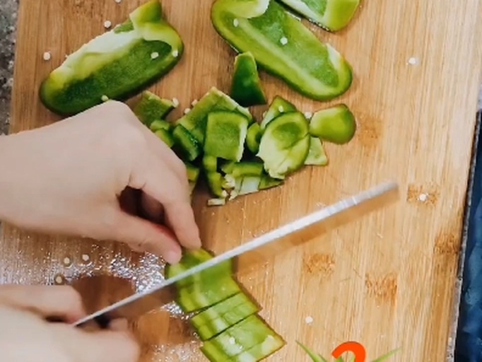 一位厨师正在案板上用刀背刮除线椒内壁的白色筋膜和籽粒,旁边摆放着整根线椒、已剖开的线椒以及切好的斜段,背景为木质厨房台面 线椒处理过程特写