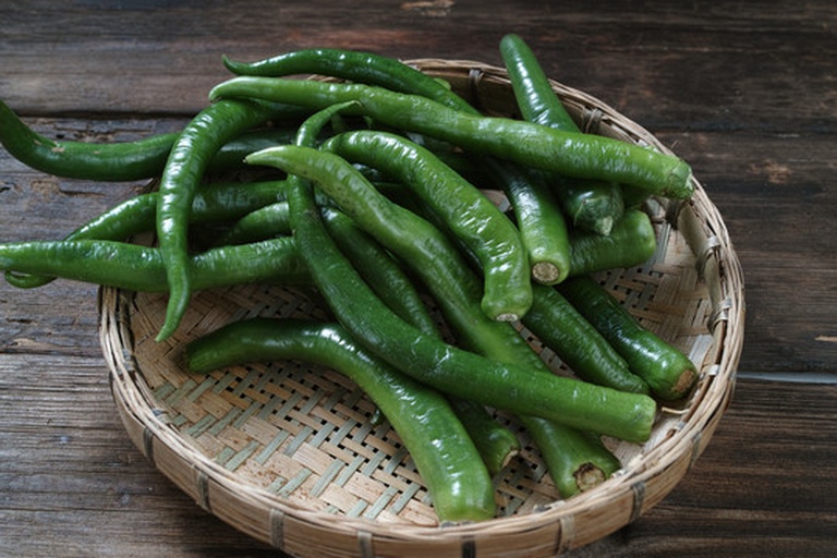 一个竹编菜篮中整齐摆放着新鲜莲藕、红胡萝卜、黑木耳干品、绿色青椒、黄色玉米棒和一段山药,背景为农贸市场摊位,阳光洒落,突出食材的自然质感与生活气息 莲藕与各类蔬菜在菜篮中的自然摆放