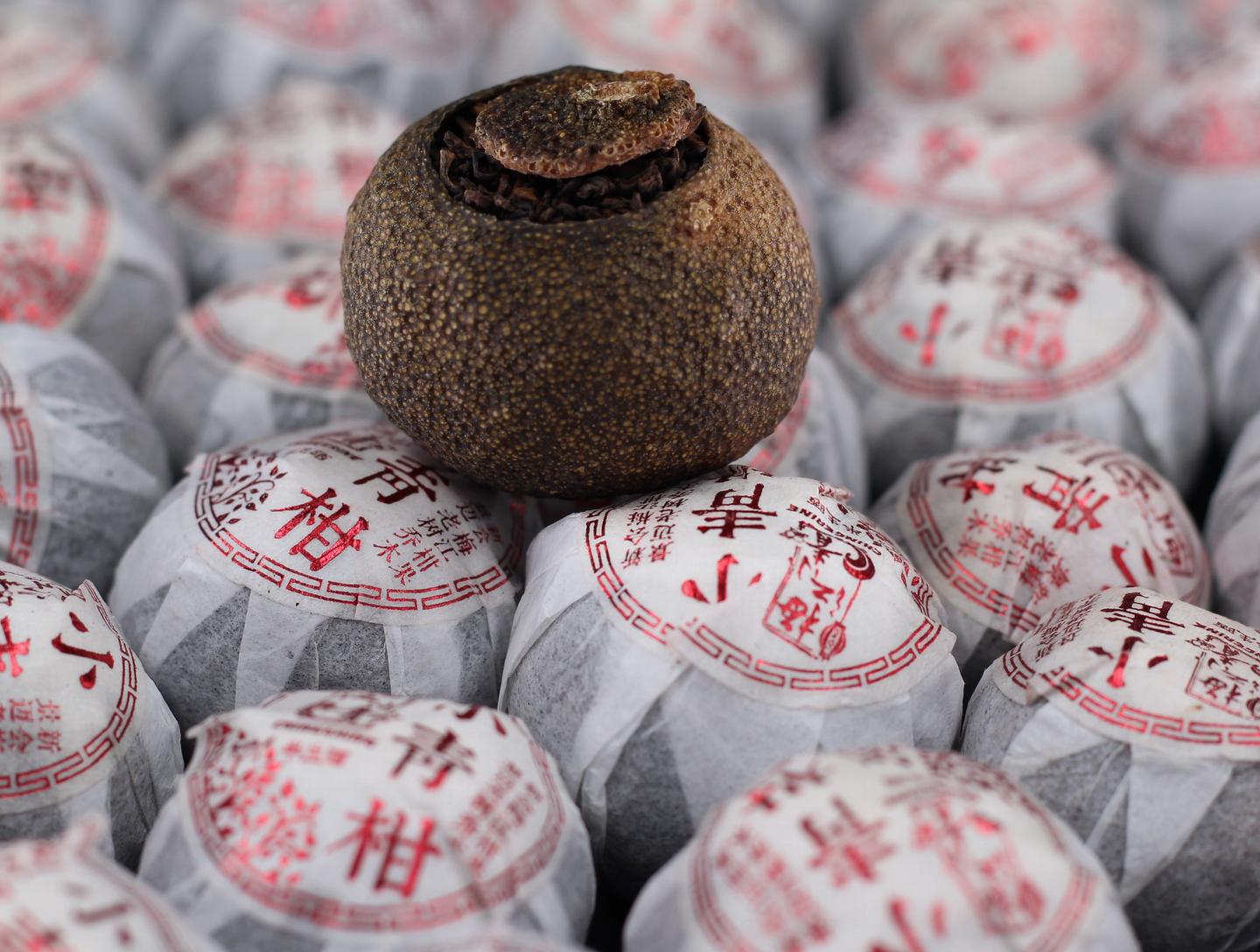 一套白瓷盖碗中正在冲泡小青柑,热水注入后茶汤呈红褐色,旁边放置一颗完整的小青柑和已拆开的空柑壳,展示茶叶填充状态,桌面铺有素色茶巾,整体画面温馨雅致 小青柑冲泡过程展示