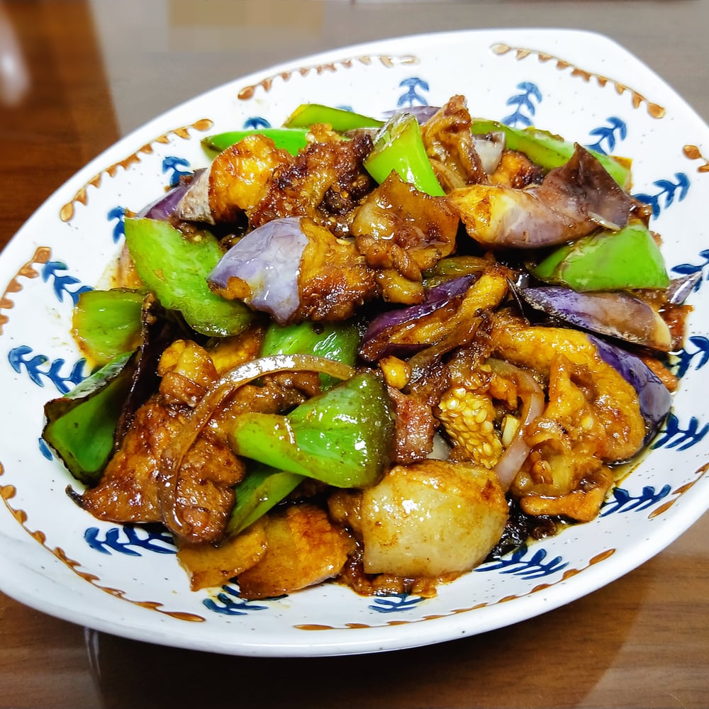 一口铁锅中正在翻炒地三鲜,茄子、土豆、青椒颜色分明,锅中酱汁浓稠适中,厨师手持锅铲进行颠勺动作,背景可见灶台火焰 图片描述