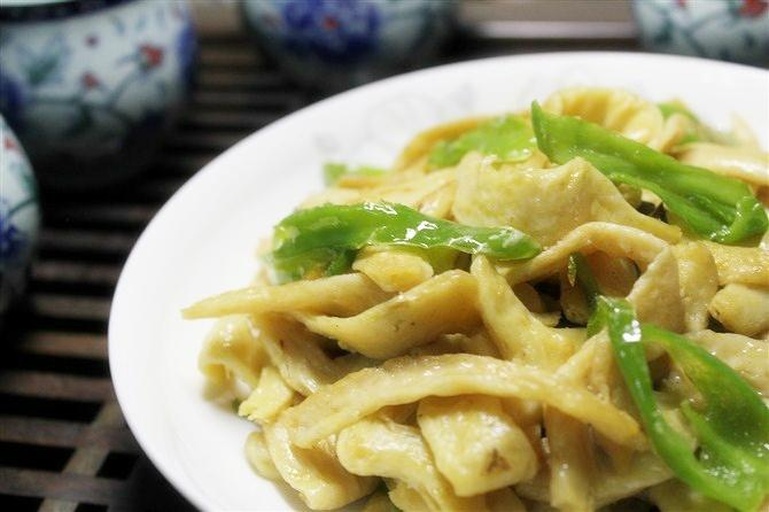 一盘刚出锅的清炒小黄瓜花,色泽碧绿鲜亮,花朵完整金黄,表面泛着淡淡油光,点缀红色椒片,盛放在白色瓷盘中,背景虚化呈现厨房灶台环境 清炒小黄瓜花出锅成菜图