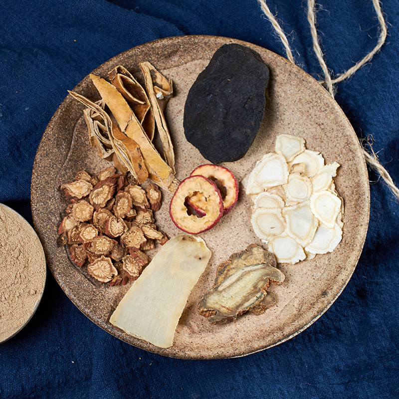 一位老药师正在传统中药房内操作铁锅炒制侧柏叶,锅中冒出淡淡白烟,手持竹帚不断翻动药材。工作台上有新鲜侧柏枝叶、已炭化的成品及标有‘侧柏炭’字样的陶瓷罐,体现传统工艺与现代规范结合的场景 传统中药炮制场景