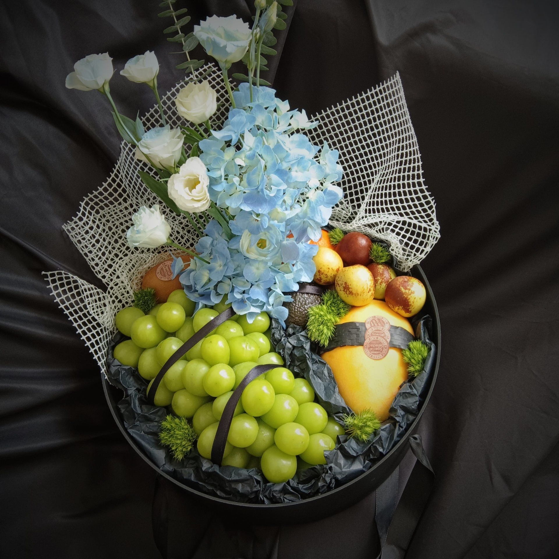 一张木质桌面上摆放着三款不同风格的爆子葡萄柚礼盒,分别为简约纸盒装、竹编提篮装和透明视窗礼盒装,每个盒子都配有品牌标签和产品介绍卡,旁边放有一杯现榨果汁和几片切开的果肉,营造出高端、健康的消费氛围 包装精美的爆子葡萄柚礼盒展示