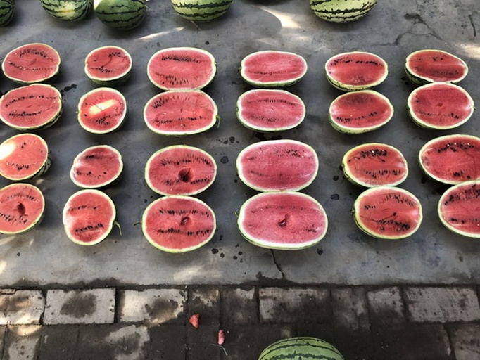 一个成熟的红籽西瓜被横向切开,露出鲜红色的果肉和整齐排列的深红色瓜籽,果汁饱满,果肉纹理清晰,背景为木质砧板,周围散落着几片西瓜瓣,光线柔和自然 红籽西瓜切开特写