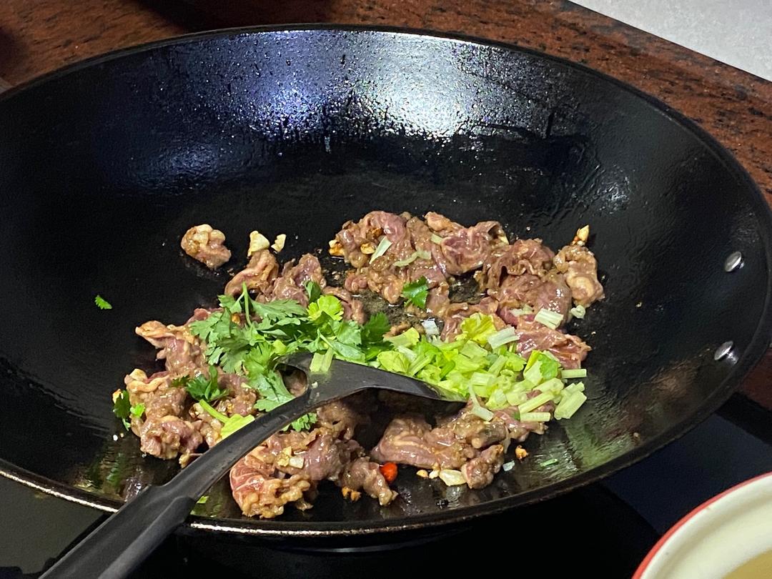 一位家庭主妇正在将几片白芷放入砂锅中炖煮牛肉,锅内热气腾腾,旁边摆放着其他香料和调料瓶,背景为整洁的现代厨房环境 厨房中使用白芷炖肉的场景