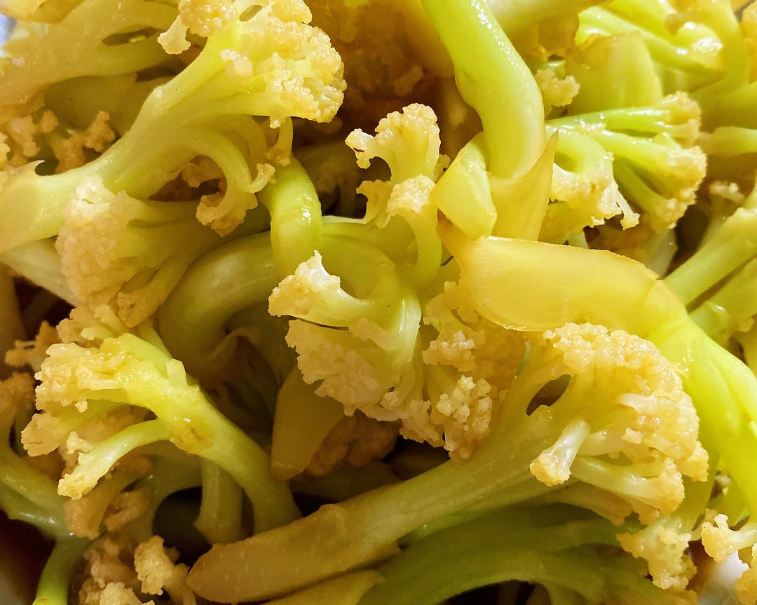 美食摄影:清炒菜花成品特写。高温快炒后天然表皮毛已完全脱落,菜花颗粒饱满、质地脆嫩、色泽清亮,体现‘菜花上有白色的毛毛’经规范处理后对最终口感与品相零影响 俯拍视角:一盘刚出锅的清炒菜花盛于青瓷盘中,菜花粒分明、色泽玉白微泛青,表面光洁无毛,配红椒丝与蒜末点缀,热气氤氲,背景虚化为厨房窗台与绿植,传递健康家常饮食氛围