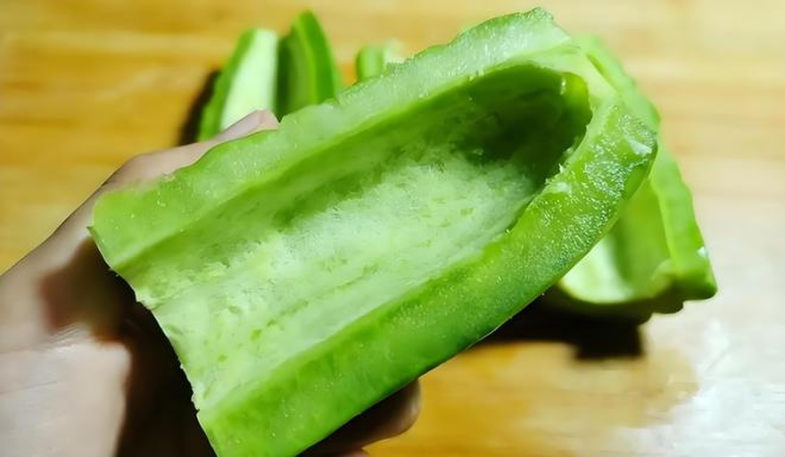 一位厨师在明亮厨房中切开一根深绿色苦瓜,刀下苦瓜露出白色内瓤和排列整齐的种子,旁边配有盐罐、滤网和碗具,展示去苦处理过程 厨房中正在处理苦瓜的场景