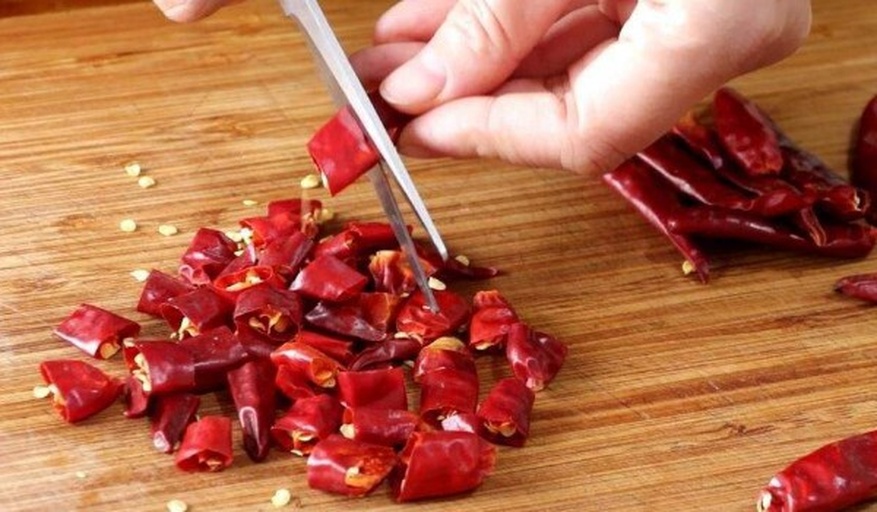 一位厨师正在用剪刀将干辣椒剪成段,锅中热油冒烟,准备炝锅,厨房环境整洁,体现干辣椒的实际烹饪用途 干辣椒在厨房中的应用场景