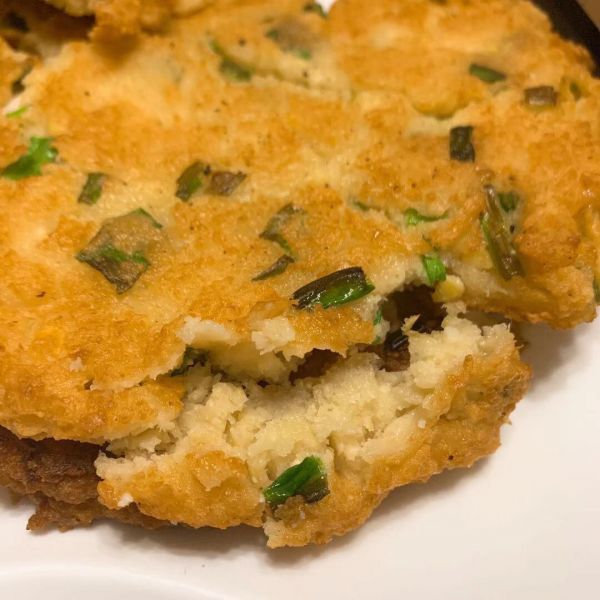 俯拍全景图:6张金黄色烀饼整齐排列于黑铁锅中,饼边微翘呈琥珀色焦边,表面隐约可见松花菜翠绿碎粒与肉馅纹理,热气氤氲,背景为东北农家土灶台,体现‘一锅出’的豪迈家常感 松花菜烀饼出锅全景