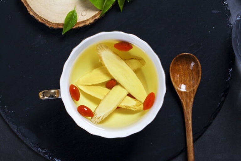 葛根片与生姜片并列摆放，旁边有正在冲泡的茶杯，热气升腾，背景为自然木质桌面