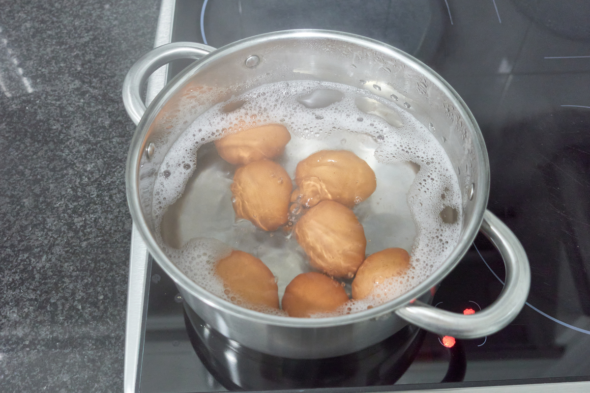 一锅正在煮制的鸡蛋,水面微沸,鸡蛋呈浅褐色,锅边有少量气泡,旁边摆放着新鲜鸡蛋和调料瓶,背景为厨房操作台 水煮蛋制作过程