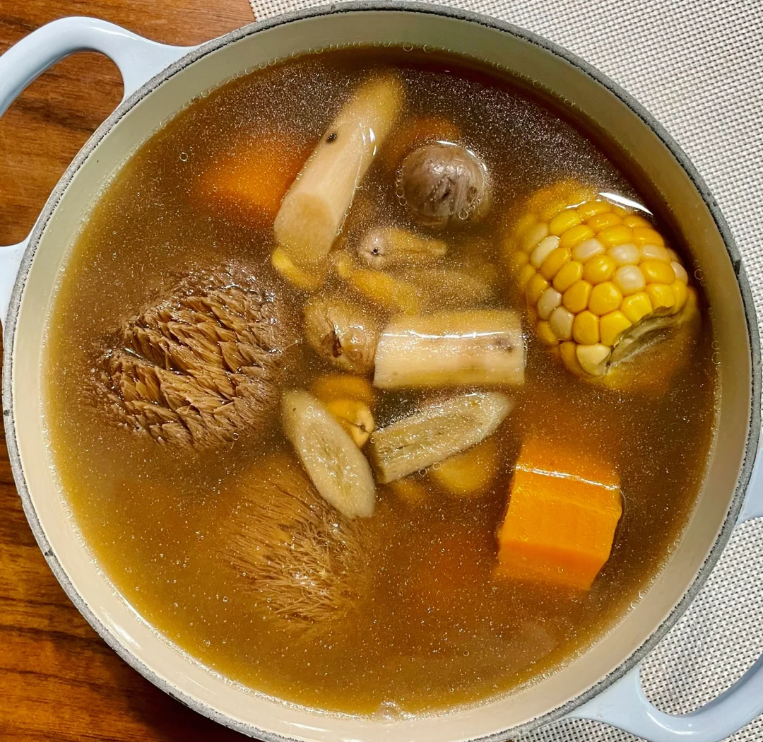 新鲜松茸、猪骨、玉米、山药等食材整齐摆放在木质案板上，背景为厨房环境，光线柔和自然