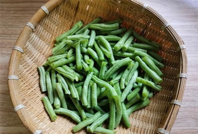 一束新鲜采摘的无筋豆,豆荚呈鲜绿色,表面光滑无斑点,整齐排列在竹编篮中,背景为田园菜园环境 新鲜无筋豆特写