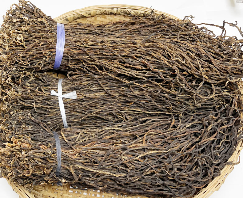 高清特写镜头下的干豆角丝产品:金黄色条状干制品整齐铺放在竹编簸箕上,背景为中国传统农家院落。右侧附有放大版营养成分表标签,清晰标注蛋白质、膳食纤维、钾、镁等核心营养指标,强调其作为功能性健康食材的价值 干豆角丝产品特写与营养标签信息展示