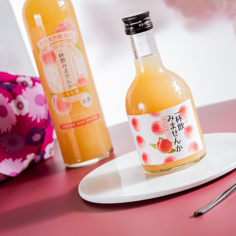商业级静物摄影:江小白蜜桃味成品酒瓶与新鲜水蜜桃果肉、绿叶、枝条组合摆放,强调产品与源头农产品的视觉关联,瓶身标签清晰可见‘4.5%vol’与‘蜜桃味’字样 江小白蜜桃味产品图:磨砂玻璃瓶身印浅粉桃枝图案、瓶内液体呈清澈淡粉色、置于水蜜桃切片与枝叶旁
