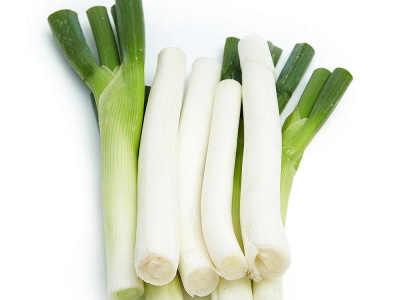 一张清晰的对比图片,左侧为一把新鲜的小葱,茎叶细长翠绿,根部略带淡白色;右侧为一根典型的大葱,葱白部分明显较长,整体更为粗壮。背景为木质厨房台面,突出食材的自然质感 小葱与大葱对比图