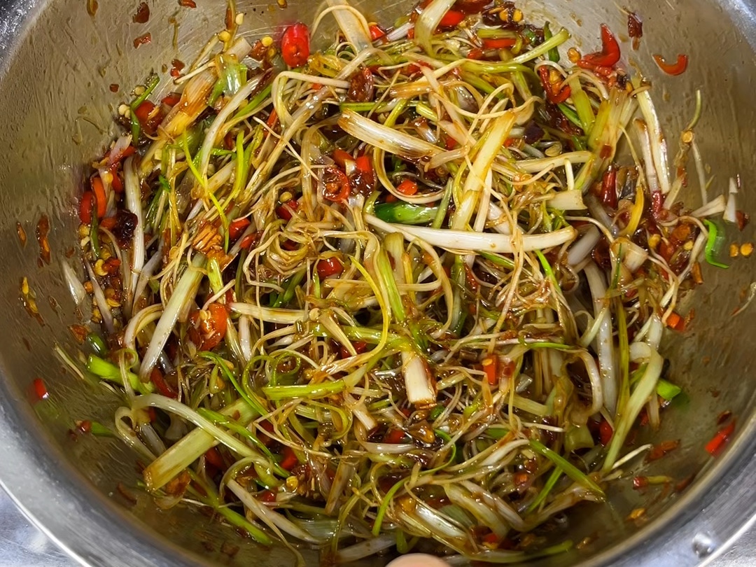 成品葱油拌面摆盘美观,突出大葱作为核心食材的应用,展现色香味俱全的美食效果 一碗热气腾腾的葱油拌面特写,面条油润发亮,上面铺满金黄色的炸葱段,旁边摆放着半根新鲜大葱和调料瓶