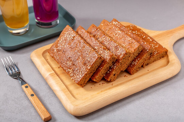 一根完整卷起的蛋糕卷置于木质托盘上,表面光滑带有淡淡粉红色,切口处可见均匀分布的草莓奶油夹心与鲜红草莓片,周围点缀散落的草莓颗粒与绿叶,背景虚化,营造温馨居家氛围 草莓奶油蛋糕卷成品展示