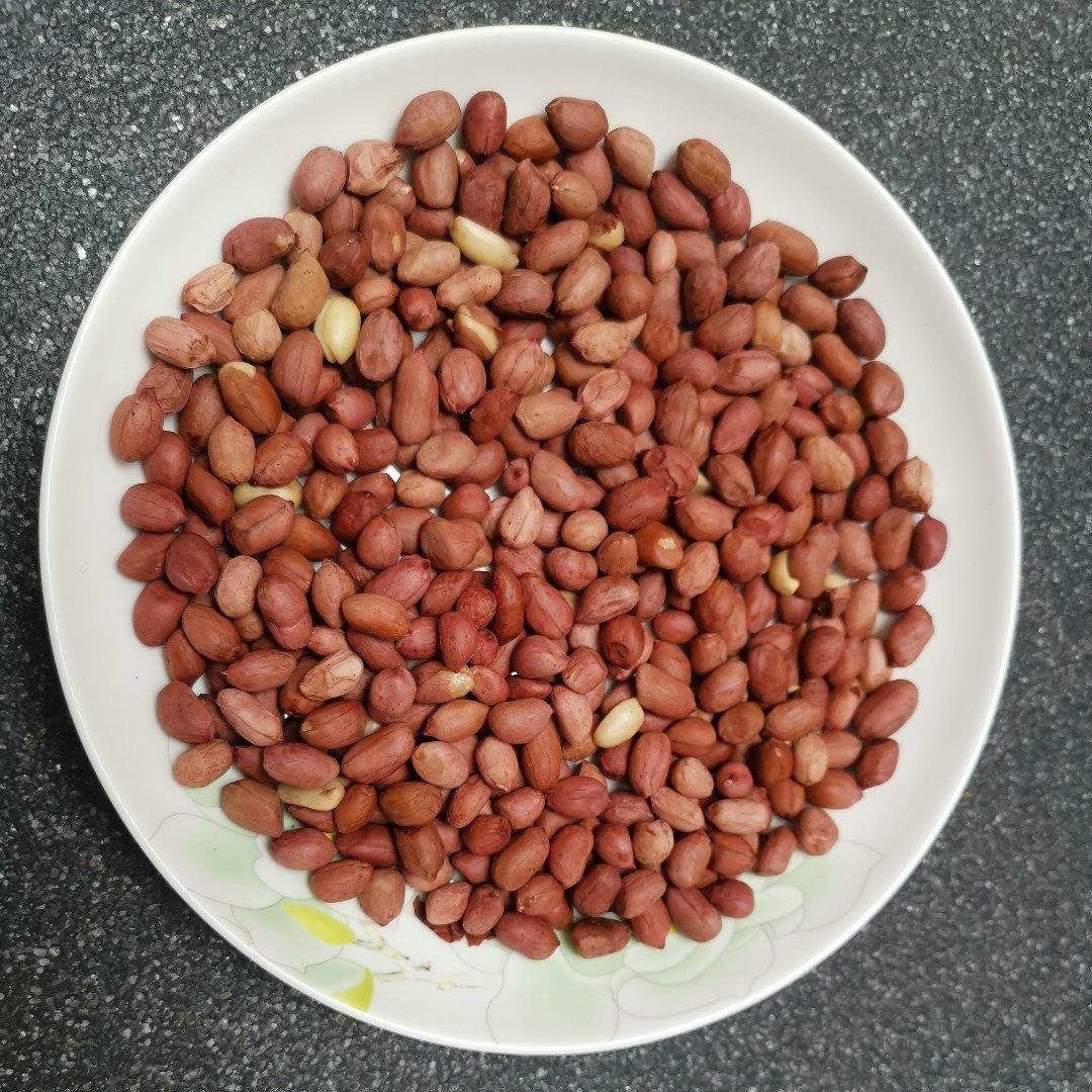 一盘刚出锅的红皮花生平铺在白色瓷盘中,色泽红亮油润,正自然冷却,背景为木质餐桌,体现家庭制作场景 炒制完成的红皮花生冷却过程