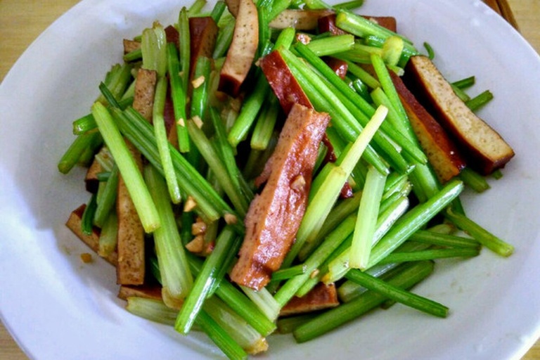 成品西芹炒香干特写：翠绿西芹段与琥珀色香干块交错分布，表面裹薄层清亮油膜，可见零星红椒丝与白芝麻点缀，热气微升