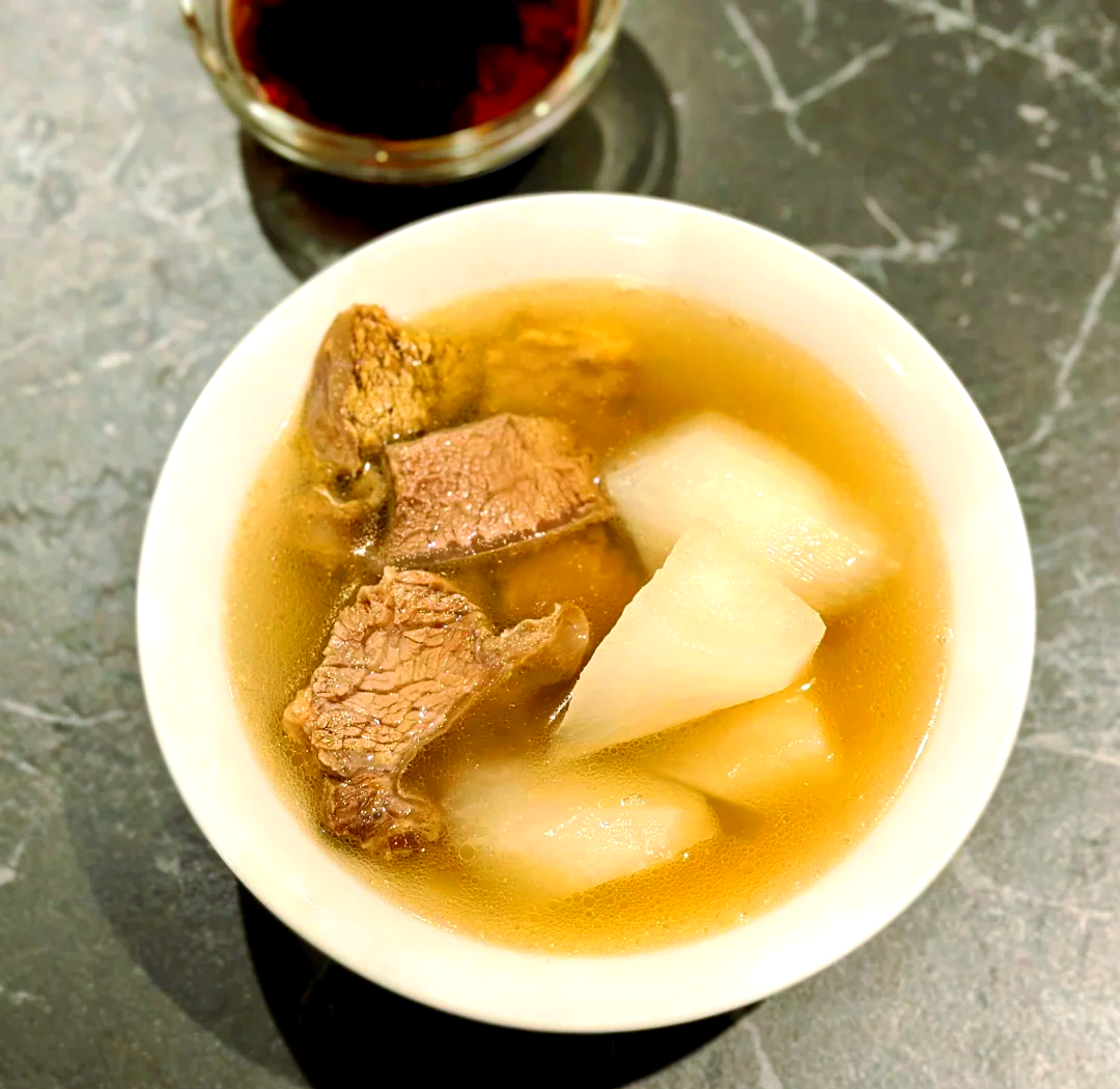 砂锅清炖牛肉萝卜汤成品图,突出汤色澄澈、萝卜晶莹、无浑浊无浮沫的视觉效果,体现‘清炖’工艺成果 砂锅中清亮琥珀色牛肉萝卜汤特写,汤面平静无浮油,可见半透明萝卜块悬浮其中,边缘微卷,几片翠绿葱花浮于汤面,背景虚化木质餐桌