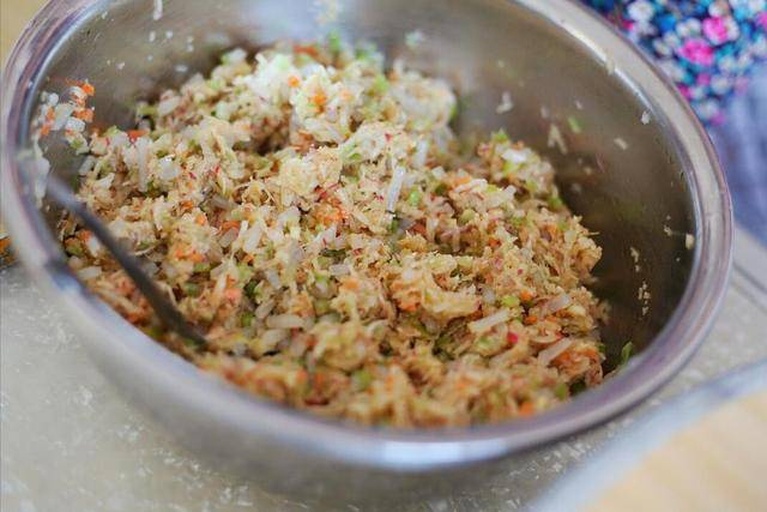 一只陶瓷大碗中正在搅拌山莴苣与猪肉混合馅料,筷子呈顺时针方向搅动,馅料呈现细腻黏稠状态,旁边摆放着切好的山莴苣碎、肉糜和调味料瓶罐 山莴苣馅料搅拌过程