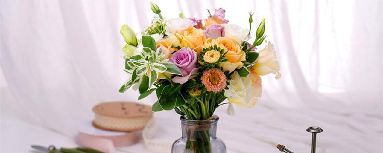 一件精美的花艺作品,中心主花为三支盛开的诺瓦利斯月季,周围搭配尤加利叶、满天星和雾中情人,整体风格清新浪漫,放置于木质桌面上,背景虚化,突出花卉的柔美色调与艺术感 诺瓦利斯月季在花艺作品中的应用