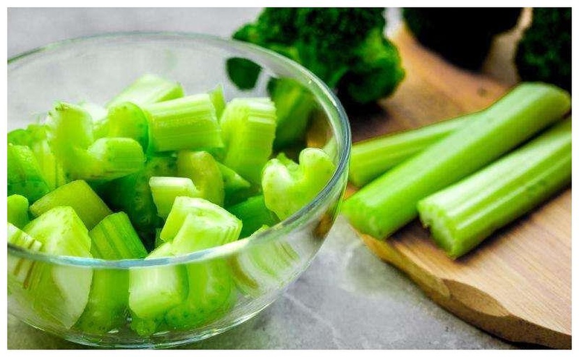 一位家庭主妇在明亮厨房中将新鲜西芹切成薄片,案板旁放有橄榄油瓶、柠檬片和蒜瓣,准备制作凉拌西芹,体现健康饮食的生活方式 家庭厨房中的西芹料理场景