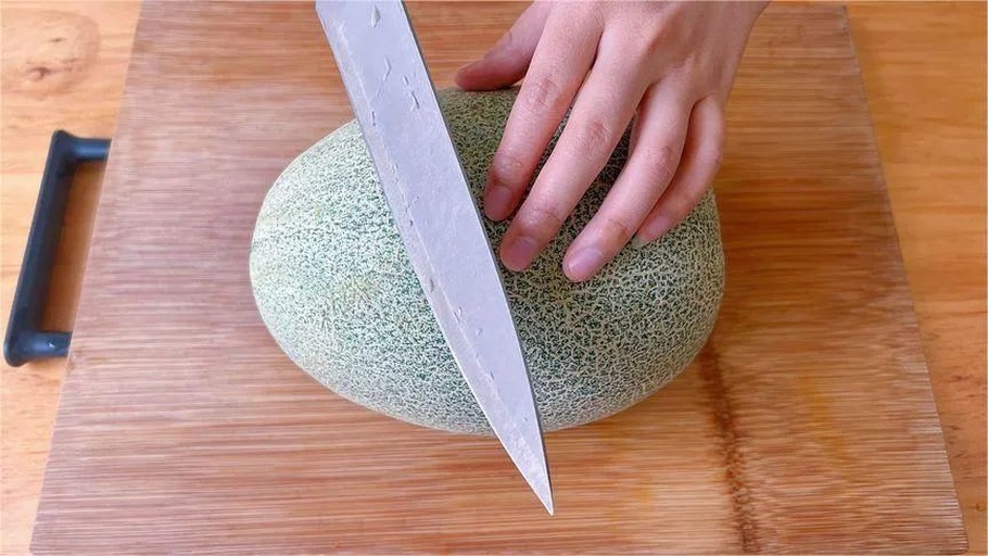 一名女性在明亮的现代厨房中操作,手拿保鲜盒正准备封盖,桌上摆放着切好的哈密瓜块,背景有料理台和调味瓶,体现日常生活场景 一位家庭主妇正在厨房将切好的哈密瓜装入透明保鲜盒,动作自然,表情专注