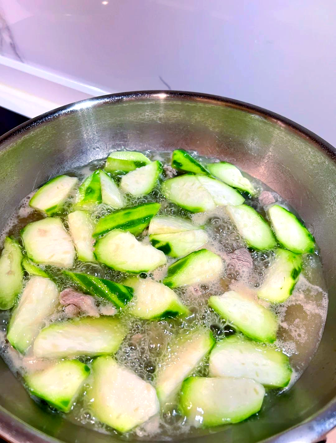 一位女性在厨房中切丝瓜，案板上有生姜和大蒜，锅中正在翻炒