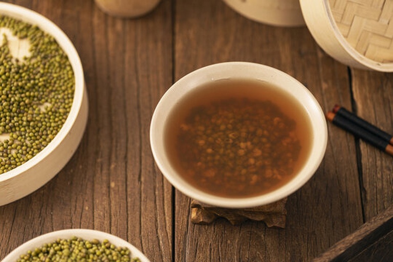 一个传统农家厨房内景,土灶上铁锅正沸腾着绿色的绿豆汤,蒸汽袅袅上升,旁边放着瓷碗和木勺,案板上有未煮的干绿豆,整体氛围温暖质朴 农家厨房熬煮绿豆汤场景