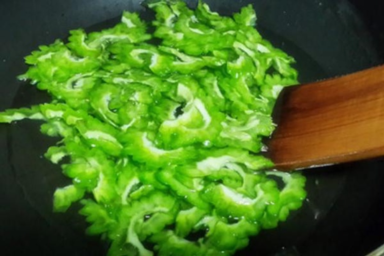 厨房中正在翻炒苦瓜洋葱绿豆混合食材的锅具场景