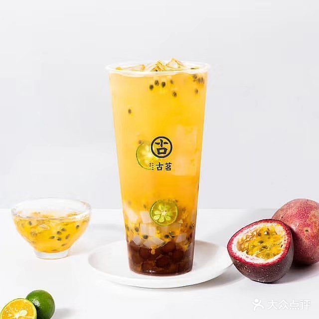 一杯冰镇金桔百香果茶特写,杯身凝结水珠,搭配柠檬片与薄荷叶,呈现清凉夏日饮品氛围 玻璃杯中盛放冰镇金桔百香果茶,杯壁有水珠,杯口插着柠檬片和薄荷叶,背景为夏日阳台绿植