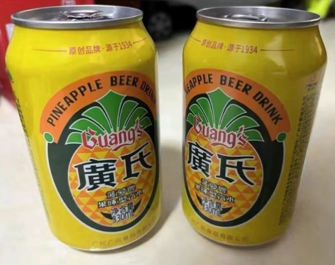 左侧为新鲜黄色菠萝果实,表皮粗糙呈鳞片状,右侧为玻璃瓶装广氏菠萝啤,标签清晰可见‘菠萝味’字样,背景为超市货架 菠萝与菠萝啤产品对比图