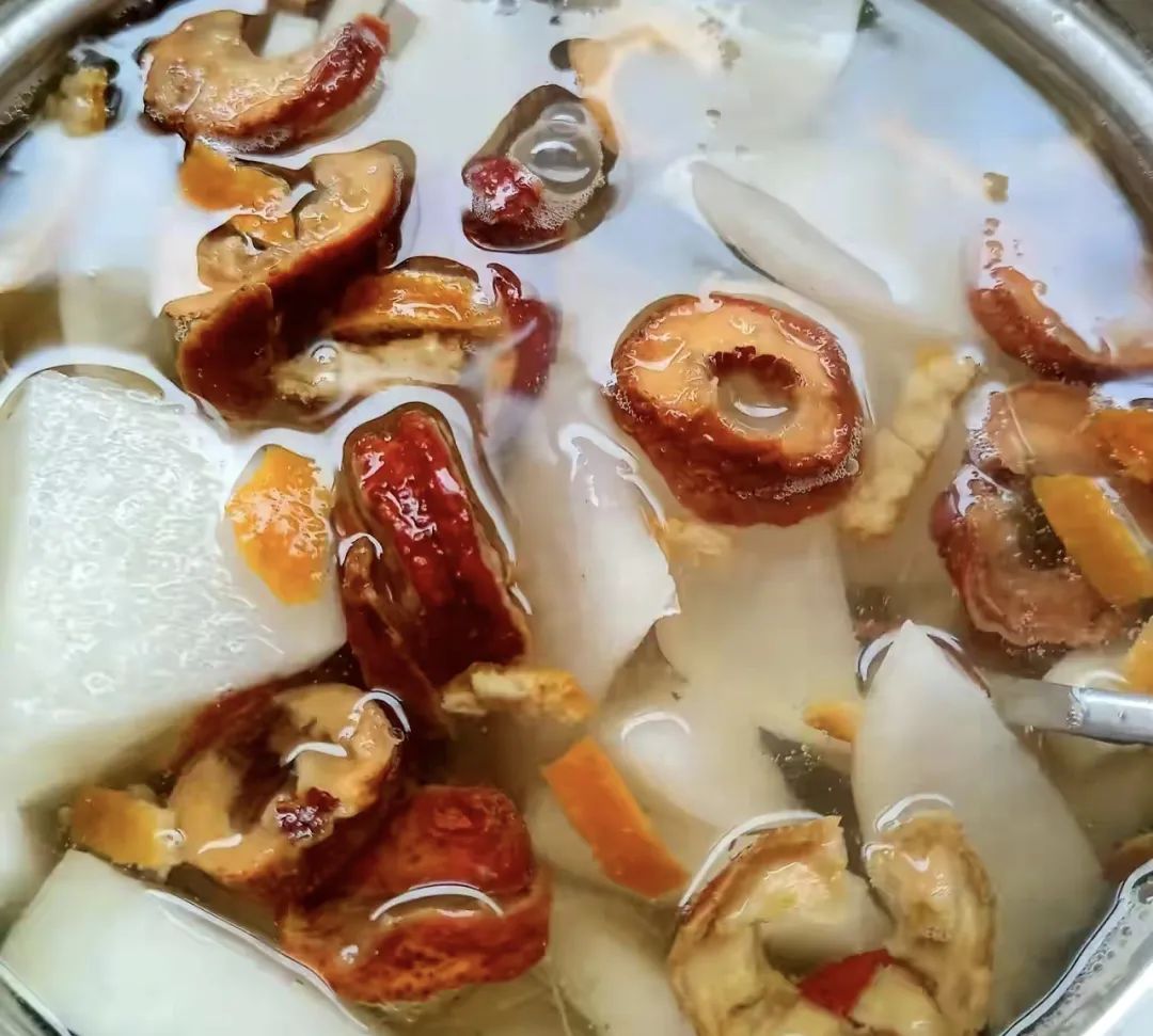 甘蔗梨大枣煮水成品图：琥珀色清亮汤汁，表面浮有细小枣皮碎屑，沉底可见梨肉纤维与甘蔗纤维絮状物，热气氤氲