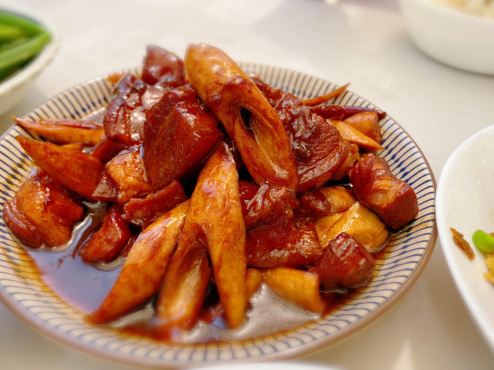 一盘刚出锅的芋头扣肉被完整翻扣在白色瓷盘中,红褐色五花肉与乳白色芋头交替排列成圆形花状,表面泛着油亮光泽,周围点缀几根翠绿葱丝,背景为木质餐桌,氛围温馨 成品芋头扣肉展示图