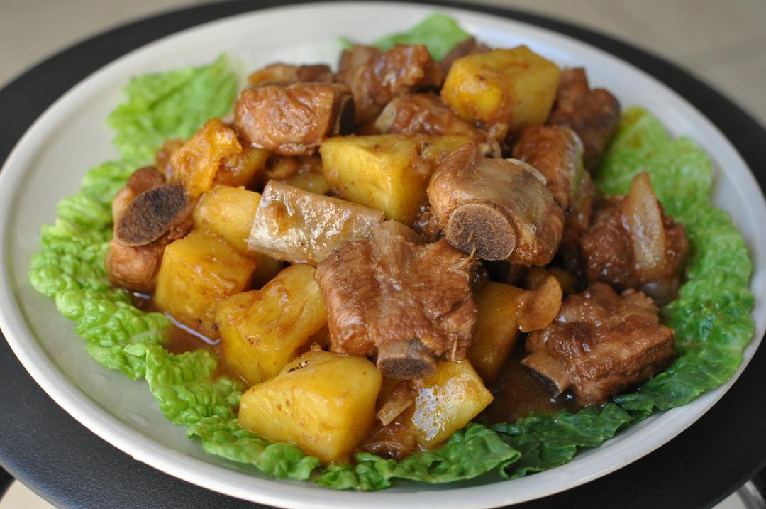 左侧为新鲜切好的菠萝块,呈金黄色三角状,整齐排列在白色瓷盘中;右侧为焯水后的猪排骨,颜色微白带粉红,表面无血沫,置于不锈钢滤网中沥干水分 菠萝切块与排骨焯水对比图