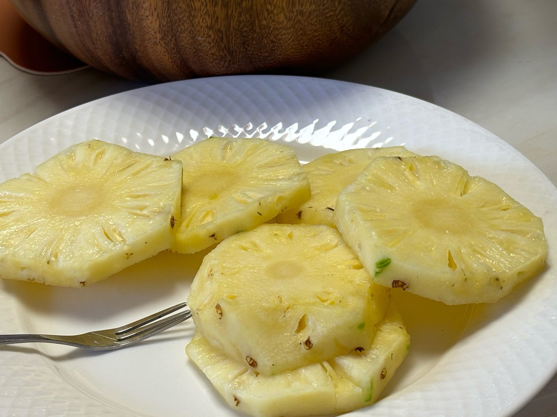 一个新鲜切开的金黄色菠萝,果肉饱满多汁,切成小块摆放在白色瓷盘中,背景为浅色木质桌面,光线柔和自然 菠萝切块特写