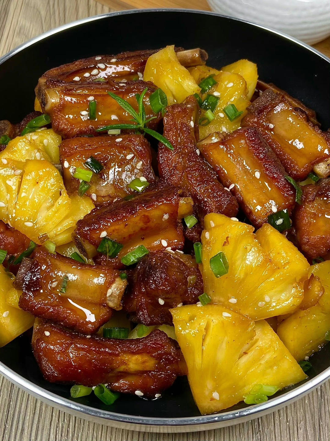 菠萝咕咾肉成品特写：金黄酥脆的肉丁裹着透亮琥珀色糖醋汁，鲜黄菠萝块与红绿彩椒错落分布，盘边点缀薄荷叶，背景为木质餐桌