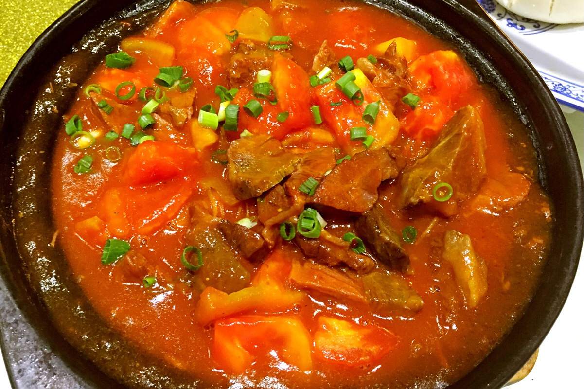 一碗热气腾腾的番茄土豆牛肉盛放在白色瓷盘中,牛肉块饱满,土豆金黄绵软,番茄融入汤汁呈琥珀红色,旁边搭配一碗白米饭,整体色彩温暖诱人 成品展示图