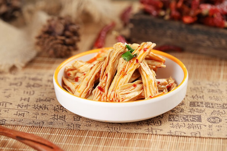 白色圆形瓷盘中盛放着刚出锅的韭菜炒腐竹,腐竹呈琥珀色,韭菜碧绿鲜亮,表面泛着自然油光,点缀少量红色辣椒丝,旁边配有竹筷一双,背景虚化体现家庭用餐温馨感 成品装盘效果