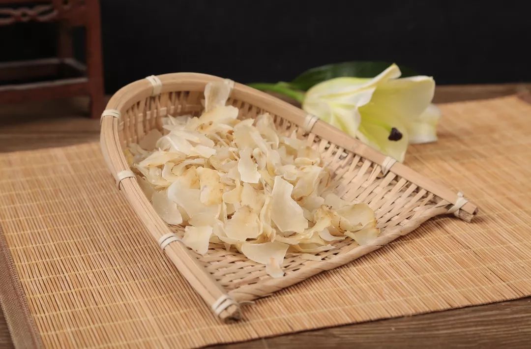 室内自然光充足的传统木构工坊中,两位二十多岁的女性并坐于原木长桌两侧:左侧女子扎低马尾,正用竹筛轻晃金黄色百合干片,细尘簌簌落下;右侧女子戴棉麻围裙,指尖轻捻一片薄如蝉翼的百合干检查脆度;桌上散落洁净瓷碗、粗陶罐与手写标签‘秋收·同心’,窗外可见晾架剪影,画面光影柔和,充满手作温度与平等协作感 百合工坊内两位女性合作筛选干燥百合片