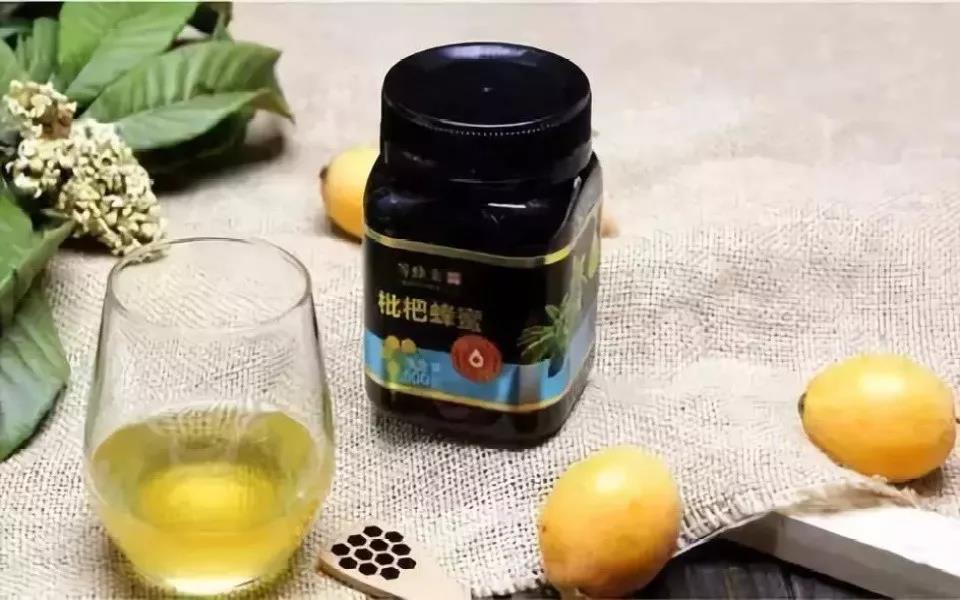 一位女性正在将一勺金黄色浓稠的川贝枇杷膏倒入透明玻璃杯中,随后注入温水搅拌,杯子旁放置一个木质托盘,上有蜂蜜罐、柠檬片和药匙,背景为温馨居家环境,传达健康养生的生活方式 川贝枇杷膏冲泡饮用示范