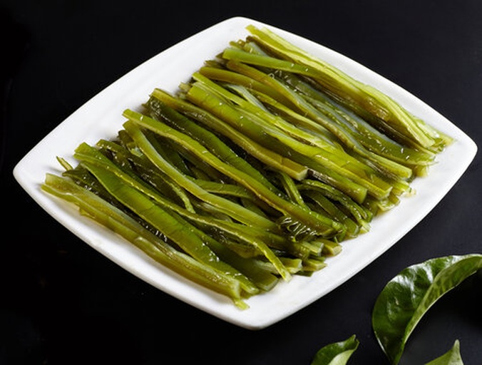 生活化场景图:明亮现代厨房中,泡发完成的干海带丝饱满舒展,色泽油润鲜亮,无发黏或断丝现象;辅料摆放有序,突出其作为健康快手菜主材的实用价值;竹筷夹取动作强化‘即用性’与‘口感韧性’感知 家庭厨房场景:不锈钢盆中盛放已泡发的深绿色海带丝,水光润泽;旁边摆放玻璃碗装芝麻酱、小碟蒜末、青红椒丝,一双竹筷正夹起一簇海带丝,展现即食凉拌准备状态