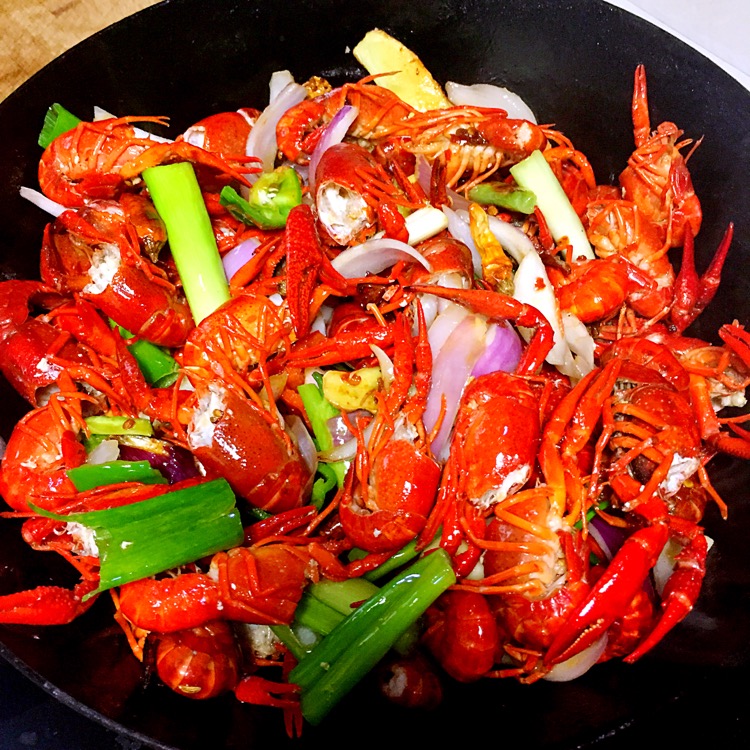 夜晚的露天大排档,桌上摆着一大盆红亮诱人的麻辣小龙虾,食客正在剥壳食用,背景有烟火气和灯光氛围,体现小龙虾作为夜宵文化的代表性食物 小龙虾在夜市大排档被端上桌