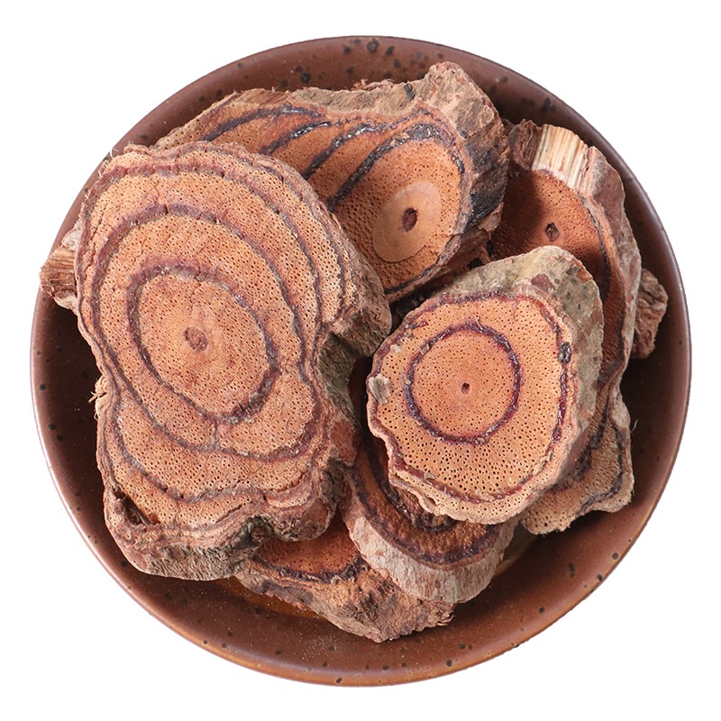 一根完整的金花梨原木横截面,展示出明显的年轮结构和金黄色至棕褐色的心材过渡,木质纹理呈波浪状交错,表面带有自然光泽,边缘保留部分树皮,背景为木质工作台 金花梨原木横切面特写