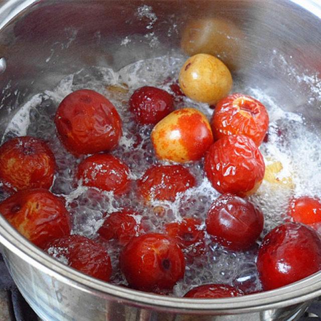 一锅正在加热的红枣水中,表面漂浮着细腻的白色泡沫,水体呈淡黄色,红枣沉于底部,锅具为不锈钢材质,背景为厨房环境 红枣煮沸过程中产生的白沫特写