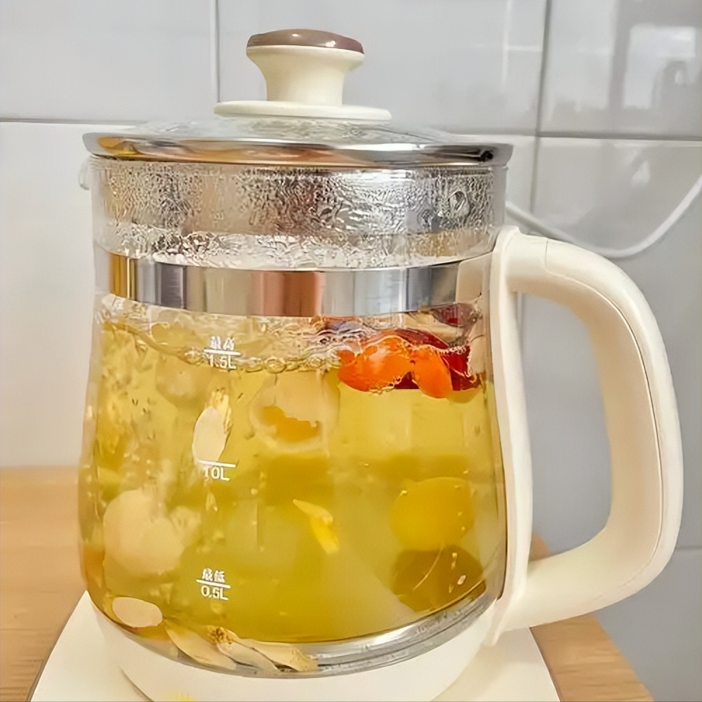 玻璃壶中正在煮沸的龙眼壳水溶液,可见数片棕褐色龙眼壳在水中翻滚,蒸汽升腾,旁边放置陶瓷杯盛有已过滤的淡黄色茶汤,桌面上散落几片干燥龙眼壳,展示家庭级健康饮品制作场景 龙眼壳煮茶过程