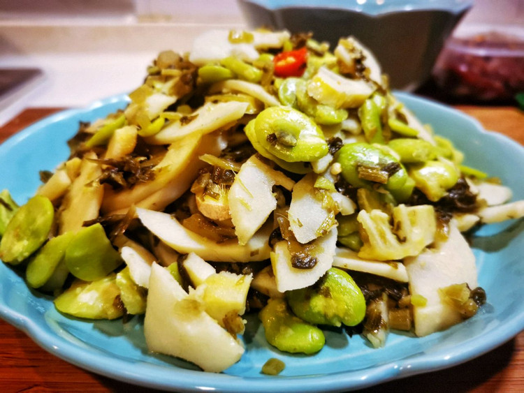 一盘刚出锅的蒸蚕豆,豆粒完整,表皮微皱,色泽青白相间,撒有少许粗盐和香葱末,旁边搭配一小碟辣椒面蘸料,餐具为粗陶碗,背景为木质餐桌,充满家常风味 蒸熟的咸味蚕豆拼盘