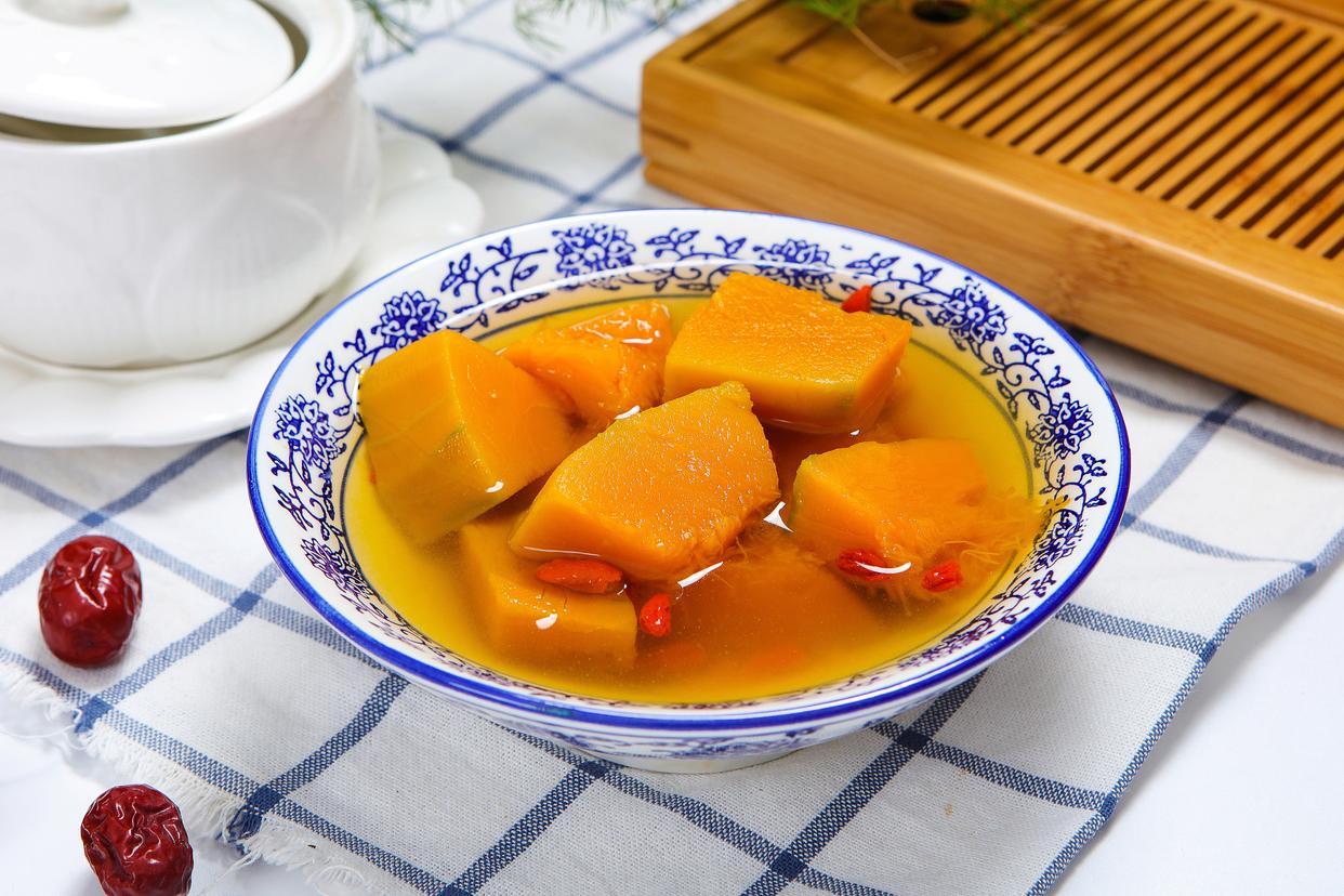一碗盛满的板栗南瓜乌鸡汤,汤色乳白清亮,乌鸡块清晰可见,橙黄色的南瓜块完整饱满,枸杞与红枣点缀其中,旁边摆放木勺和绿色薄荷叶装饰,背景为原木餐桌 成品板栗南瓜乌鸡汤盛入汤碗的摆拍图